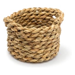 Small round natural khous woven basket holding four lipsticks on a light wooden nightstand next to a bed. - view 2
