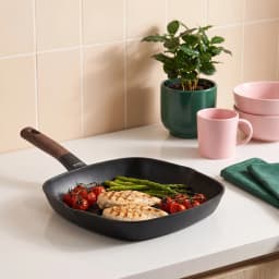 Black square granite grill pan with a dark brown wood-look handle, 28 cm, on a white shelf. - view 1