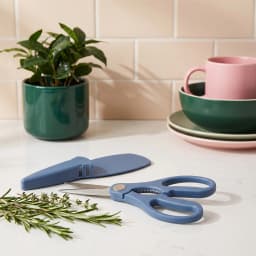 Blue kitchen scissors with silver metal blades and a blue protective sheath, resting on a white background. - view 1