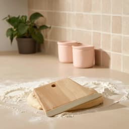 Light brown wooden dough scraper with a beige plastic blade and a hanging hole, on a white background. - view 1