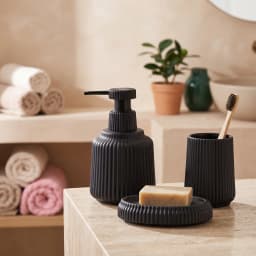 Three black ribbed ceramic bathroom accessories: a soap dispenser, a tumbler, and a soap dish on a white background. - view 1