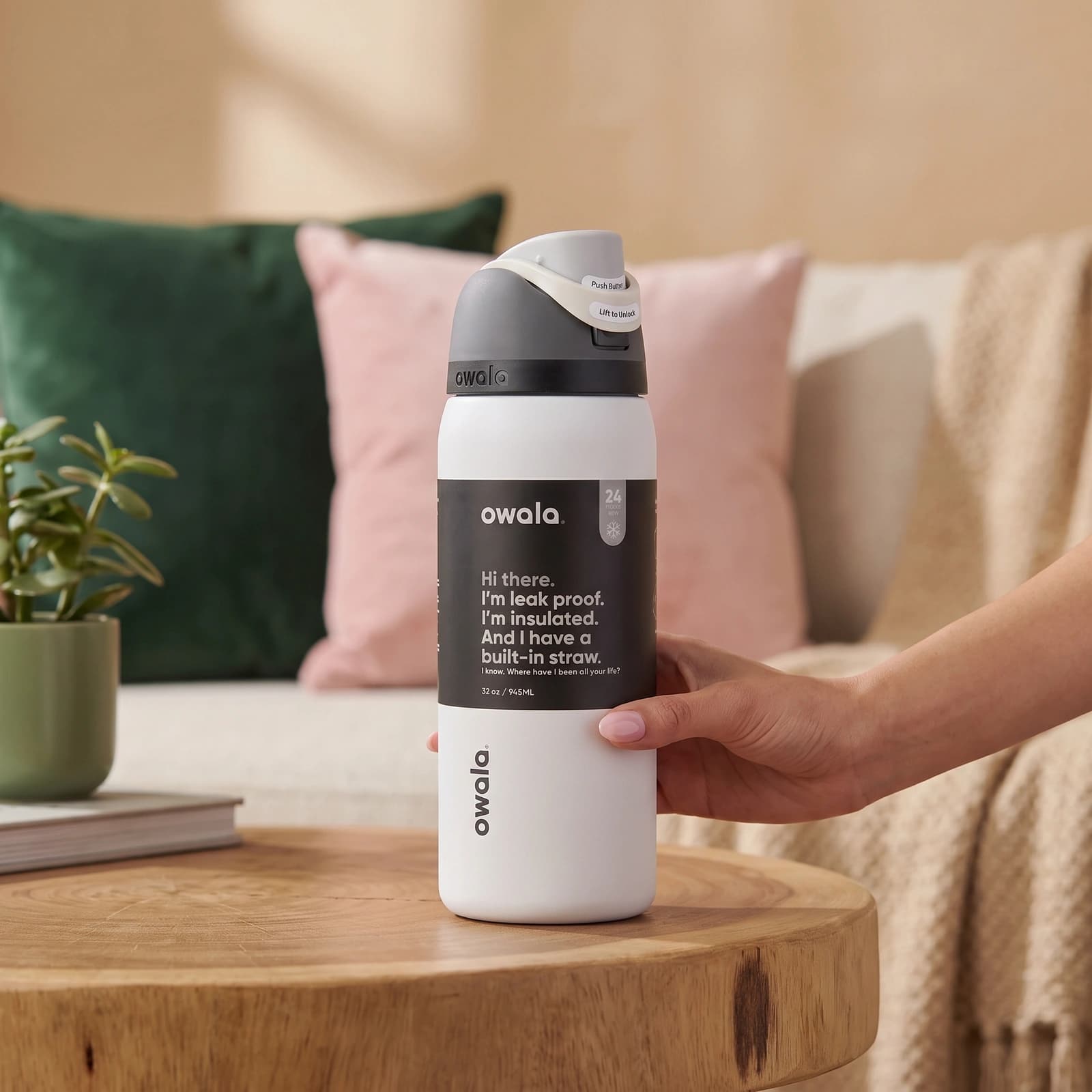 White insulated water bottle with a grey and black lid, featuring a push-button straw mechanism, on a light wooden shelf.