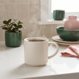 Single off-white ceramic mug with chevron pattern holding steaming coffee on a kitchen counter - view 1