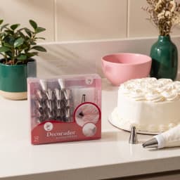 Boxed set of 25 silver metal cake decorating nozzles, a white piping bag, and a coupler, displayed on a shelf. - view 4