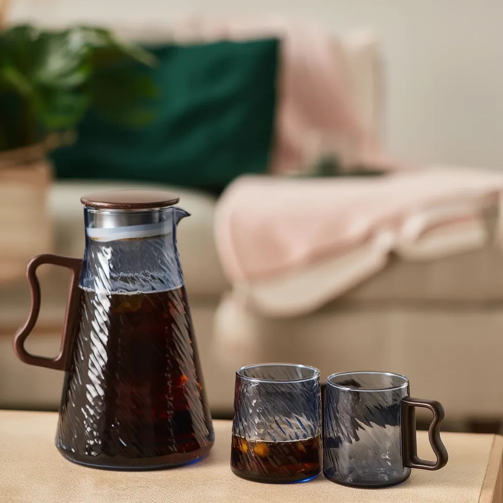 Blue textured glass pitcher with brown lid and handle, alongside one matching glass and one mug, filled with cold beverage.