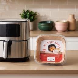 Stack of 100 brown square paper air fryer liners in clear plastic packaging on a white shelf - view 1