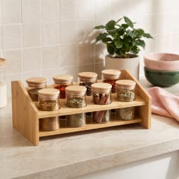 Eight clear glass spice jars with light brown wood lids on a two-tier natural wood storage rack on a white background. - view 1