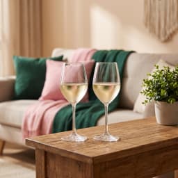 Two clear stemmed glass wine glasses in a brown and purple cardboard box, one glass is outside the box. - view 1