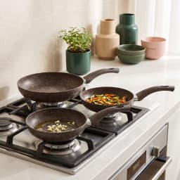 Three nested speckled brown granite frying pans with matching ergonomic handles on a white background. - view 1