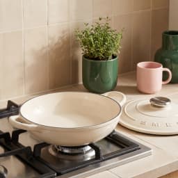 Beige cast iron braiser with a clear knob lid and two side handles, 26 cm diameter, on a white surface. - view 1