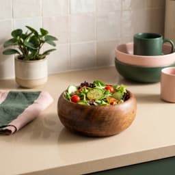 Dark brown wooden salad bowl filled with fresh green salad, cucumbers, and cherry tomatoes on a light countertop. - view 1