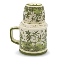 Cream porcelain jug with green floral pattern and matching cup inverted on top, on a kitchen counter. - view 2
