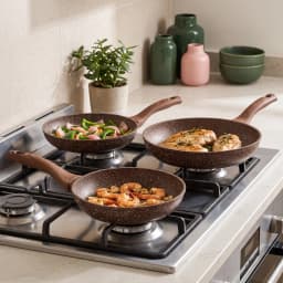 Two brown speckled granite fry pans with wood-look handles, one nested inside the other, on a kitchen counter with garlic an… - view 1