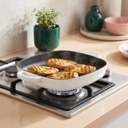 Square white and black cast iron grill pan with ribbed interior and two loop handles on a white background. - view 1