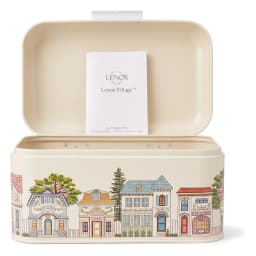 Cream metal bread box with a hinged lid, decorated with a colorful village scene illustration on a white background. - view 3