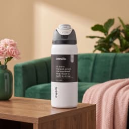 White insulated water bottle with a grey and black lid, featuring a push-button straw mechanism, on a light wooden shelf. - view 3