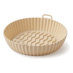 Single round beige silicone air fryer basket liner with wavy bottom and two small handles on a white shelf. - view 2