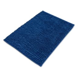 Dark blue rectangular shaggy bath mat on light brown tiled bathroom floor, with a wooden cabinet and rolled towels in backgr… - view 3