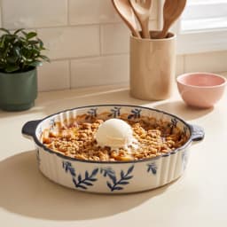 Cream round porcelain baking dish with dark blue leaf pattern and black handles, 12 inches, on a white surface. - view 1