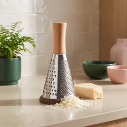 Silver metal conical grater with a light brown wooden handle and a dark brown silicone base on a white background. - view 1