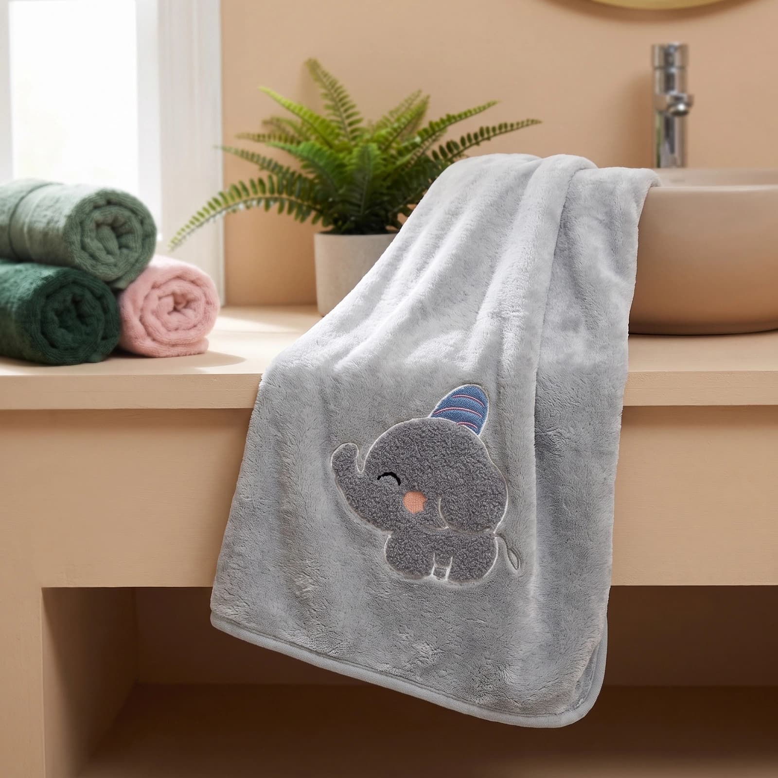 Folded grey microfiber towel with an embroidered cute grey elephant wearing a blue and pink striped hat