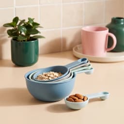 Set of four nested plastic measuring cups in shades of blue, green, and grey, with handles, on a white background. - view 1