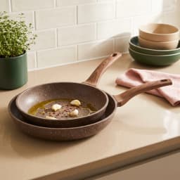 Two brown speckled granite fry pans with wood-look handles, one nested inside the other, on a kitchen counter with garlic an… - view 4