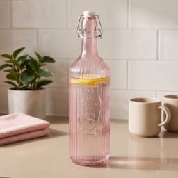 Single pink ribbed glass bottle with a white ceramic and metal swing top stopper on a white background. - view 1