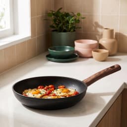 Black granite frying pan with a dark brown wooden handle, viewed from an angle on a white background. - view 1