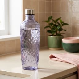 Transparent grey glass bottle with a wavy textured design and a silver metallic cap, standing on a white shelf. - view 1