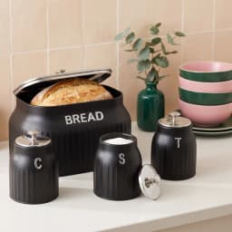 Four-piece black porcelain kitchen storage set with silver lids and knobs, including a bread bin and three canisters labeled… - view 1