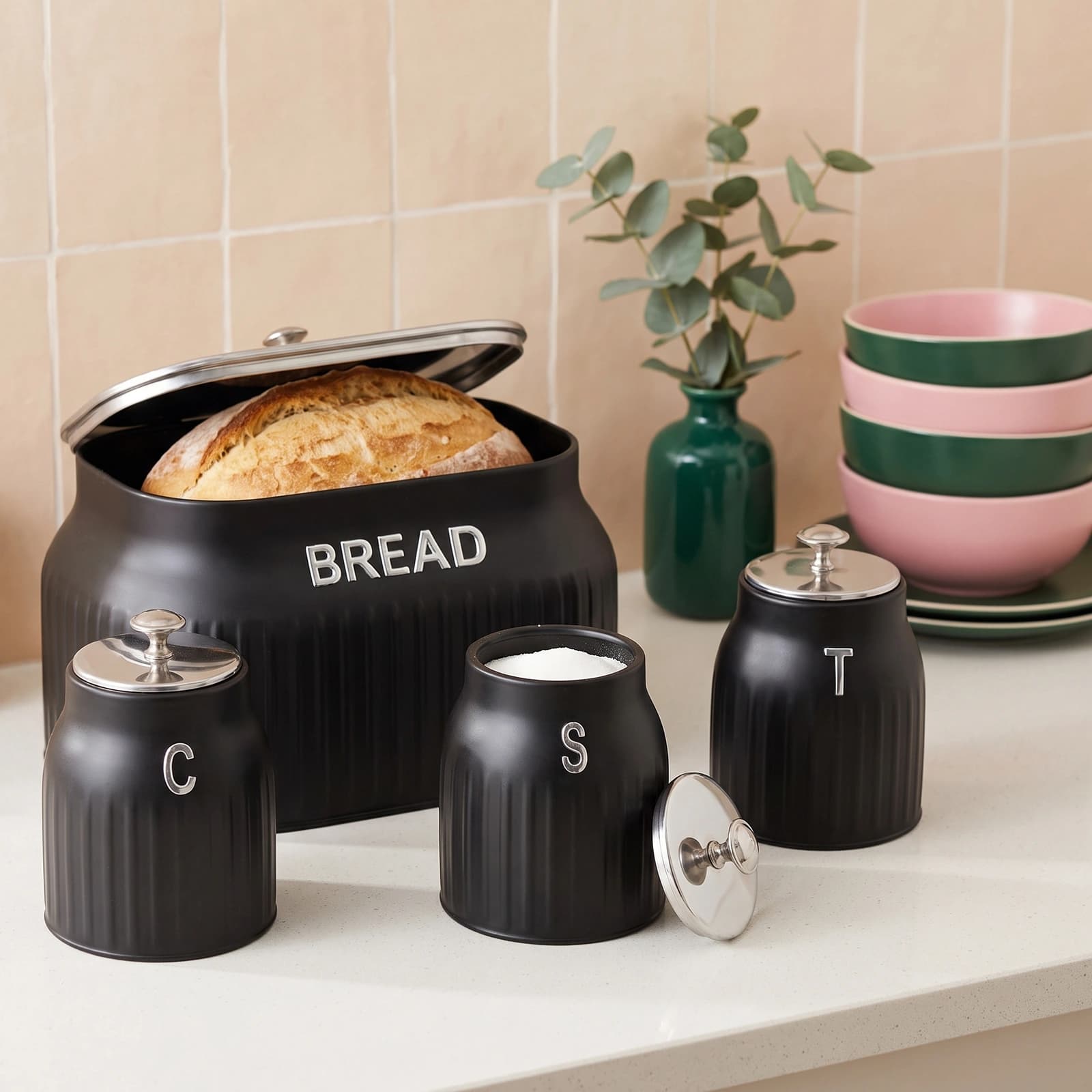 Four-piece black porcelain kitchen storage set with silver lids and knobs, including a bread bin and three canisters labeled…