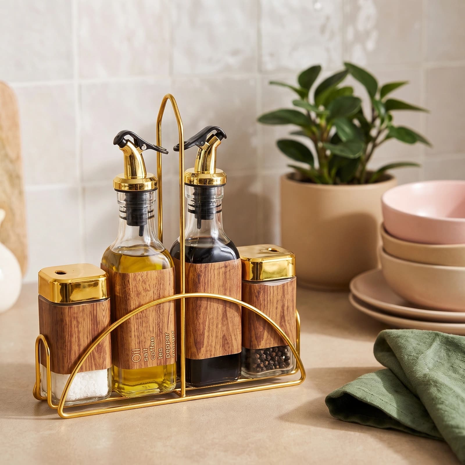 Four-piece clear glass oil and spice set with gold tops and wood-look labels, in a gold metal stand on a white background.