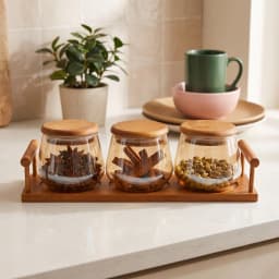 Three clear glass storage jars with round light brown wood lids, sitting on a rectangular dark brown wood tray with handles,… - view 1
