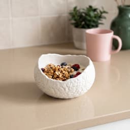 White porcelain serving bowl with an organic, textured exterior, filled with yogurt, granola, and berries on a kitchen count… - view 1