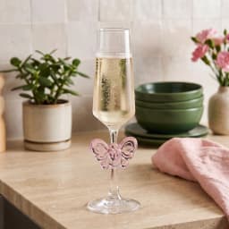 Clear glass champagne flute with a slender stem and base, featuring a translucent pink butterfly decoration on the stem. - view 3