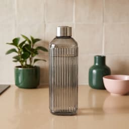 Tall smoked grey ribbed glass bottle with a silver metallic cap, standing upright in white foam packaging. - view 1