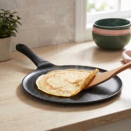 Round dark grey granite non-stick crepe pan with a black plastic handle on a white surface - view 1