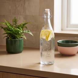 Clear ribbed glass bottle with a white swing top lid and metal clasp on a white background - view 1