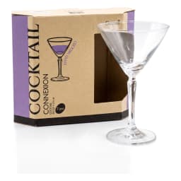 Two clear glass cocktail glasses with green liquid on a wooden table next to a plant and product box, with sofa in backgroun… - view 3