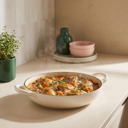 Beige cast iron braiser with a clear knob lid and two side handles, 26 cm diameter, on a white surface. - view 3