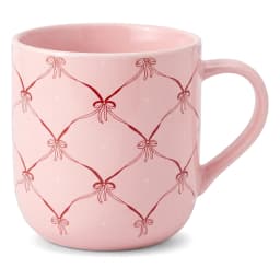 Hand holding a light pink ceramic mug with a red bow and small heart quilted pattern against a blurred background of other m… - view 2