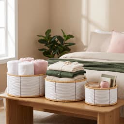 Set of three round khous storage baskets in white and natural colors, holding rolled towels, folded clothes, and books on a… - view 1