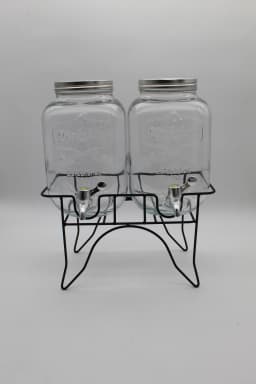 Two clear glass beverage dispensers with silver lids and spigots on a black metal stand against a white background. - view 2