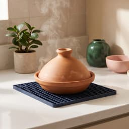 Square navy blue silicone grid coaster under a steaming terracotta tagine on a white kitchen counter - view 1