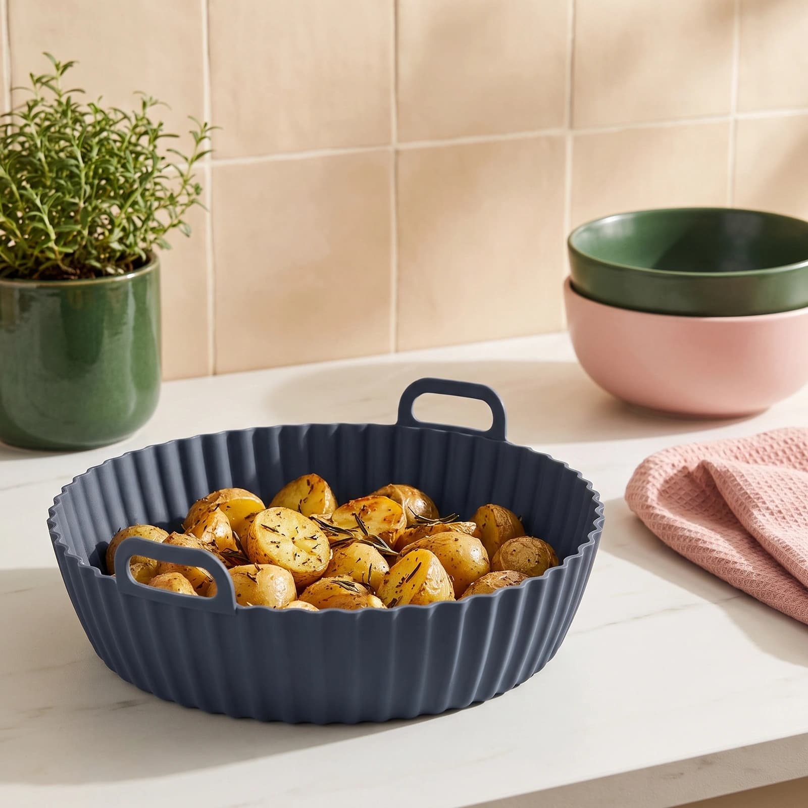 Round dark grey silicone air fryer liner with wavy bottom and fluted sides, featuring two small handles, on a white shelf.