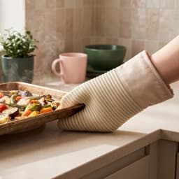 Single beige and light pink silicone and fabric oven mitt with a ribbed palm, resting in a white styrofoam tray. - view 1