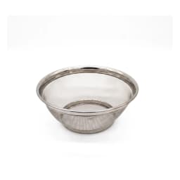 Silver stainless steel mesh colander bowl filled with red cherry tomatoes and green basil leaves on a light kitchen counter. - view 2