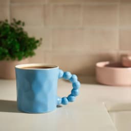 Single light blue ceramic mug with a unique handle made of connected spherical shapes, on a white background. - view 1