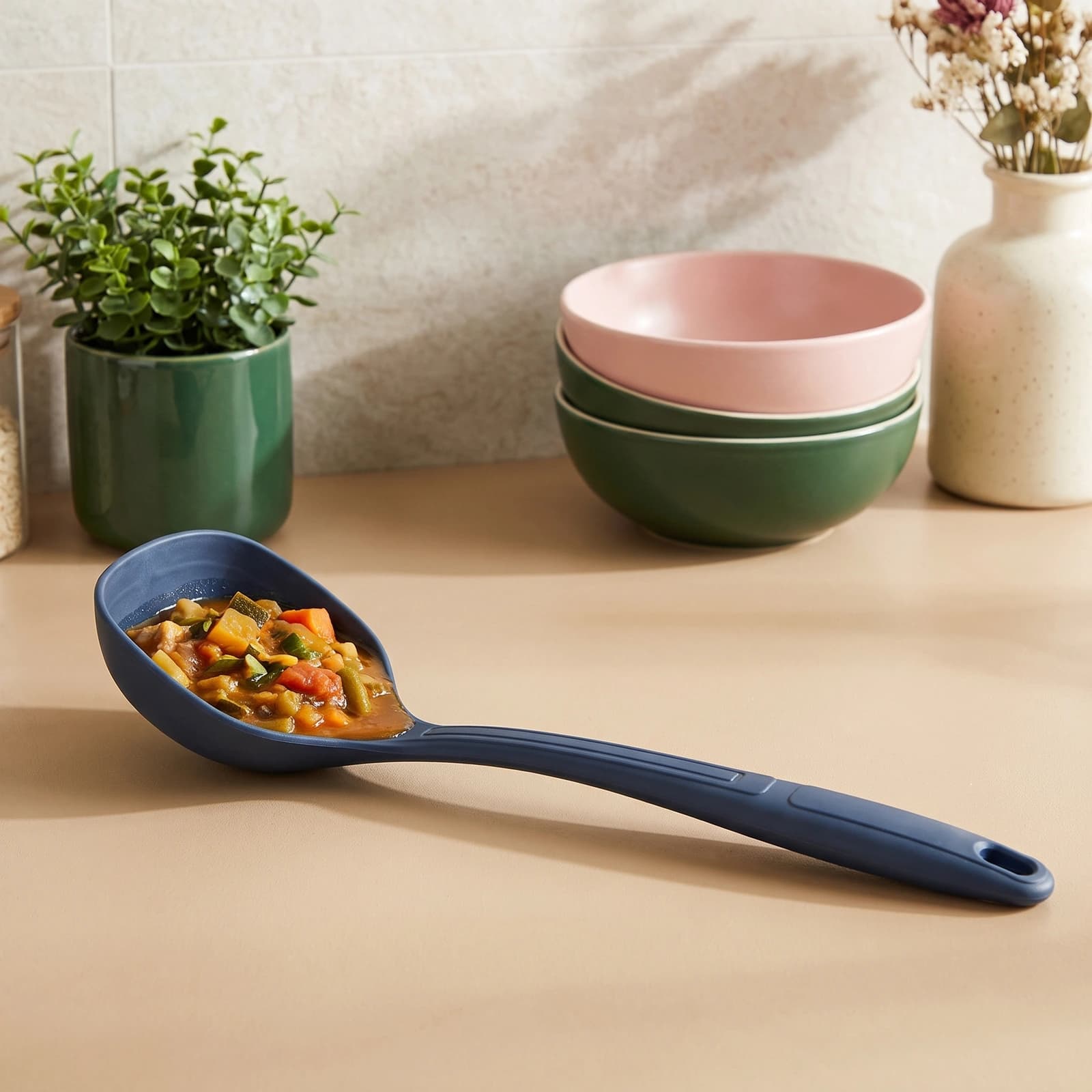 Single dark blue silicone ladle with a ribbed handle and hanging hole, standing upright on a white shelf.